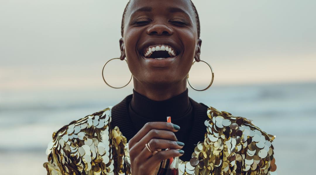 closeup of woman with big smile, gold earrings and gold sequined jacket looking successful and joyful