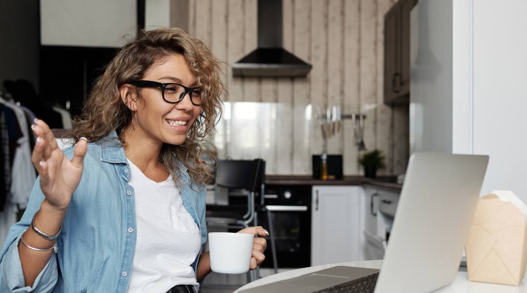 smiling woman with coffee cup chatting on computer video 