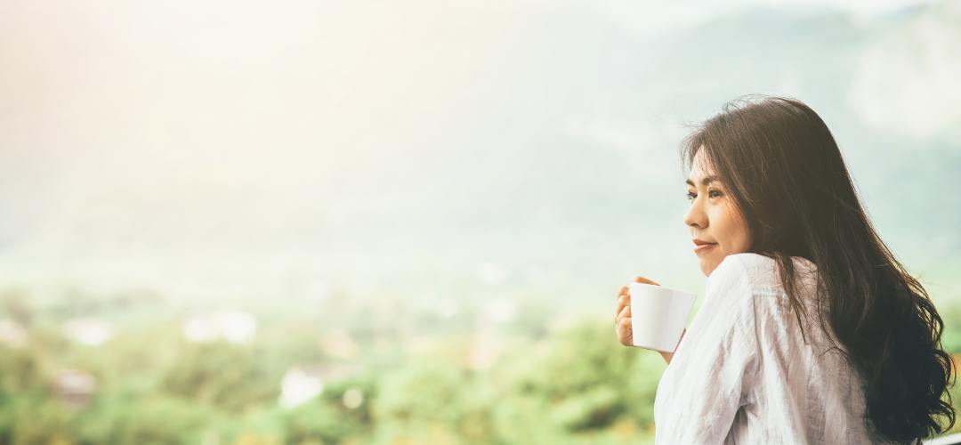 Woman enjoying time freedom with cup of coffee, looking out over a green landscape