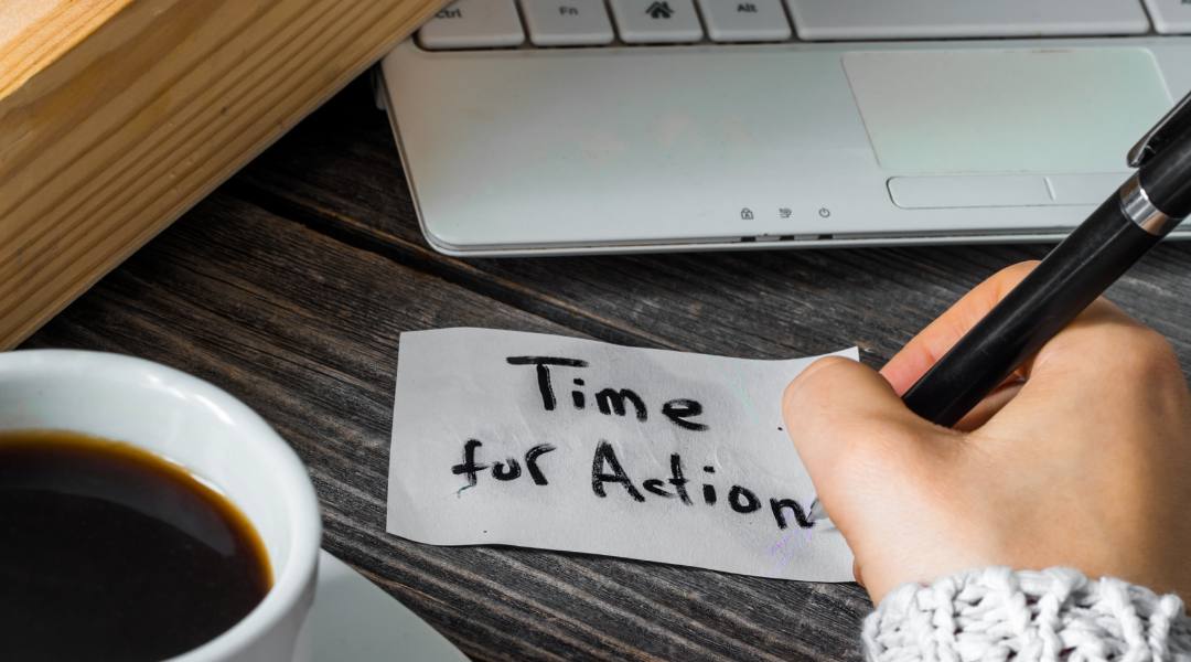 handwritten note on desk with text, "time for action". laptop keyboard in background.